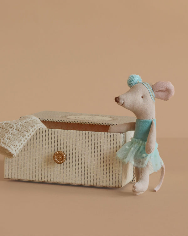 The Maileg Dance Mouse in Daybed, Little Sister - Mint features a little mouse in a mint dress and headband standing beside a cream-striped daybed with lace cloth, displayed against a beige background.