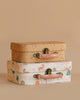 The Maileg Unicorn with Suitcase Set features two stacked vintage-style suitcases: the top is tan with a floral pattern, and the bottom is white with pink handles and playful animal and nature designs, set against a beige background.
