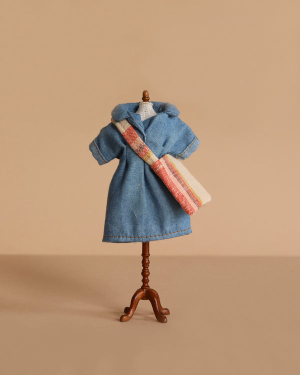 The Maileg Extra Clothing: Denim Dress And Bag for Mum Mouse features a stylish denim dress with short sleeves and a hood, plus a striped shoulder bag—perfect accessories to showcase mouse clothes against a plain beige background.