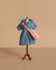 The Maileg Mum Mouse Wardrobe Set features a miniature mannequin displaying a blue collared, short-sleeve coat and a cream shoulder bag with red and orange stripes, all set against a beige background.