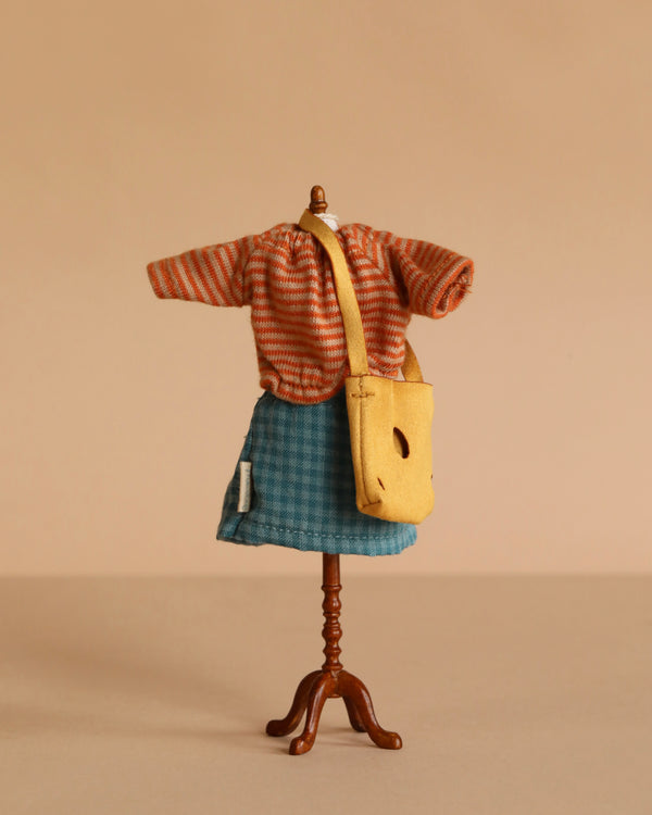 A Maileg Extra Clothing set for Mum Mouse is displayed: an orange striped top, blue plaid skirt, and yellow bag are shown against a beige background.