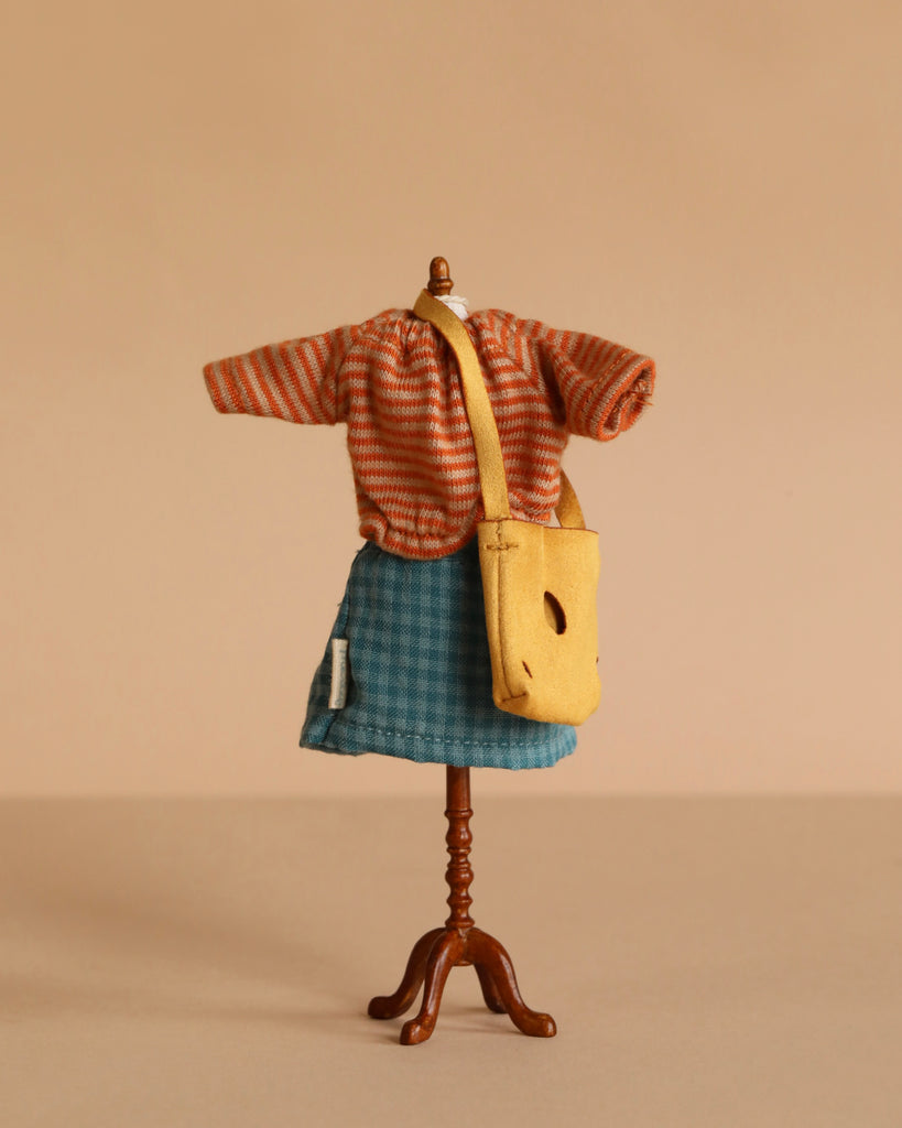 A Maileg Extra Clothing set for Mum Mouse is displayed: an orange striped top, blue plaid skirt, and yellow bag are shown against a beige background.