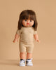 The Minikane Standing Doll (14") - Chléa With Clothing features straight brown hair, a beige knit outfit, and white sneakers with black laces. This anatomically correct doll is made in Spain and stands against a plain beige background.