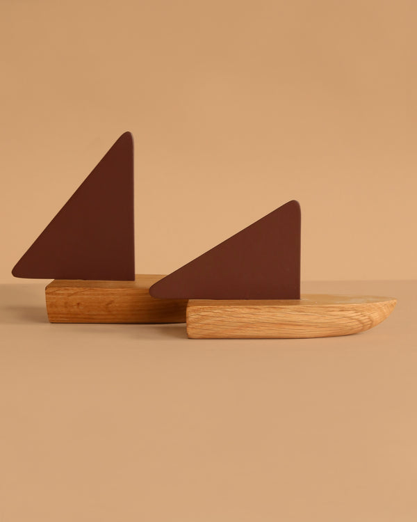 The Ferm Living Opty Boat - Set of 2 features abstract decorative boats with FSC certified oak bases and dark brown triangular sails, shown against a beige background for a timeless design accent.