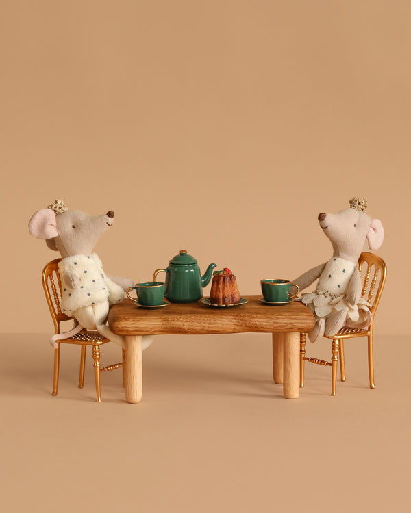 Two Maileg Royal Twin Mice in crowns and capes sit at the Maileg Royal Dining Set—a golden table with a green teapot, cups, and cake—creating a charming Christmas tea party scene against a plain beige background.