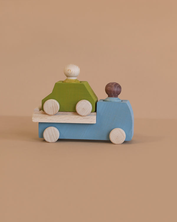 The Lubulona Wooden Tow Truck - Grey carries a green toy car with two peg people, perfect for small-world play, displayed on a plain beige background.