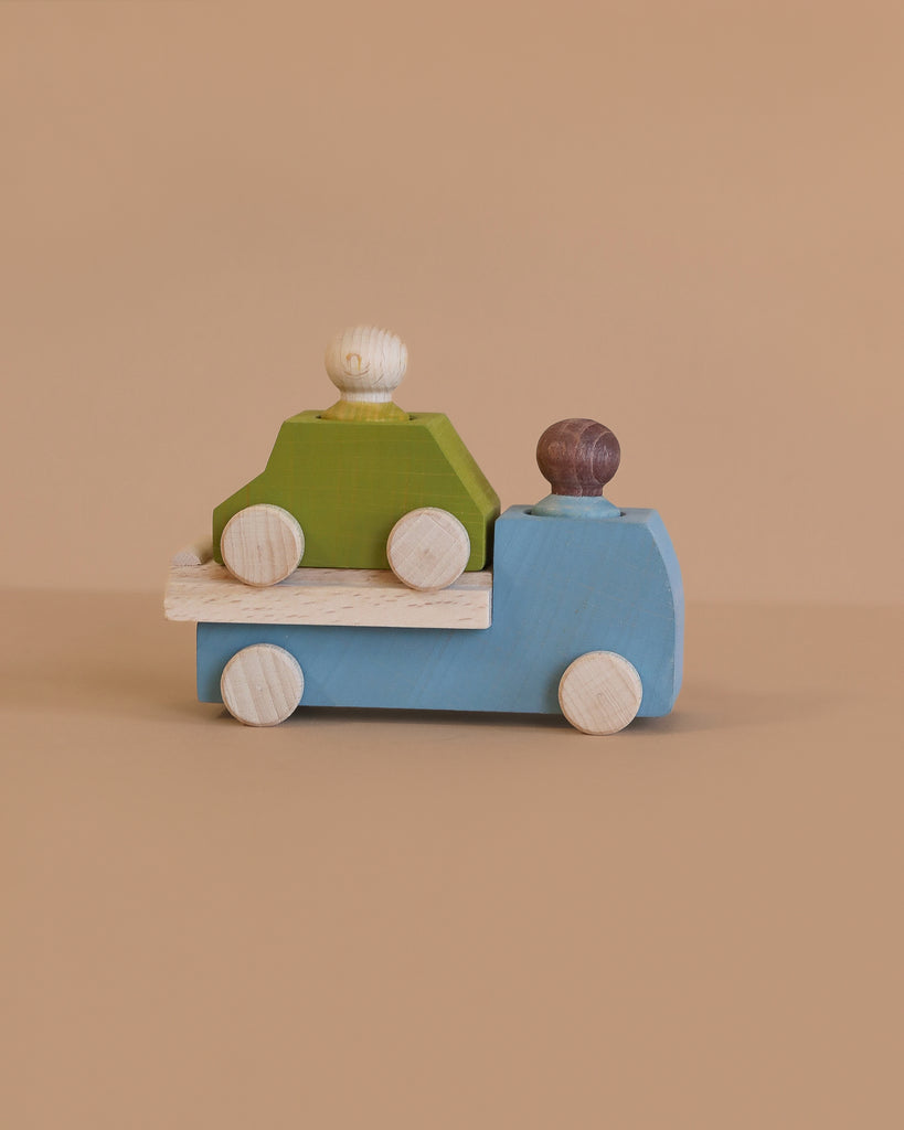 The Lubulona Wooden Tow Truck - Grey carries a green toy car with two peg people, perfect for small-world play, displayed on a plain beige background.