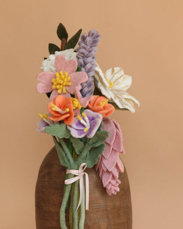 The Handcrafted Felt Flower Bouquet showcases pink, white, orange, purple, and green wool felt blooms in a brown vase with a light pink ribbon—an eco-friendly gift set against a plain beige background.