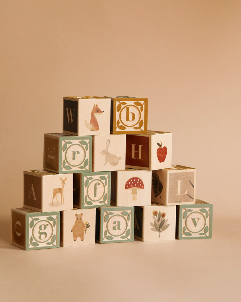 The Newborn Gift Set features a pyramid of watercolor ABC blocks crafted from sustainable basswood, each with a letter and illustrations—fox, rabbit, bear, mushroom, strawberry, flower—on a beige background.