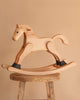 The Spring Copenhagen Wooden Rocking Horse - Final Sale is displayed on a rustic wooden stool, highlighting Nordic style against a simple beige backdrop.