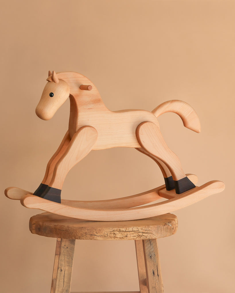 The Spring Copenhagen Wooden Rocking Horse - Final Sale is displayed on a rustic wooden stool, highlighting Nordic style against a simple beige backdrop.