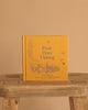 The yellow hardcover "Winnie-the-Pooh: Pooh Goes Visiting" stands upright on a rustic wooden stool against a beige background, featuring blue illustrations of Winnie-the-Pooh and friends on the cover.