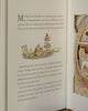 A page from *The Brambly Hedge Pop-Up Book by Jill Barklem* displays an illustrated table with teapots, cups, fruit, and cakes as Mrs. Apple enjoys an autumn walk and receives an invitation to a cozy mouse home from Primrose Woodmouse.