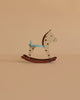 The Maileg Rocking Horse, Mouse - Spotted features brown rockers, a white body with brown spots, and light blue accents, making it a delightful dollhouse accessory. Displayed against a plain beige background.