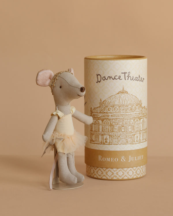 The Maileg Ballet Dancer Mouse, Big Sister, wearing a yellow ballet outfit, stands next to a cylindrical box labeled "Dance Theater Romeo & Juliet," which shows a theater illustration on a beige background.