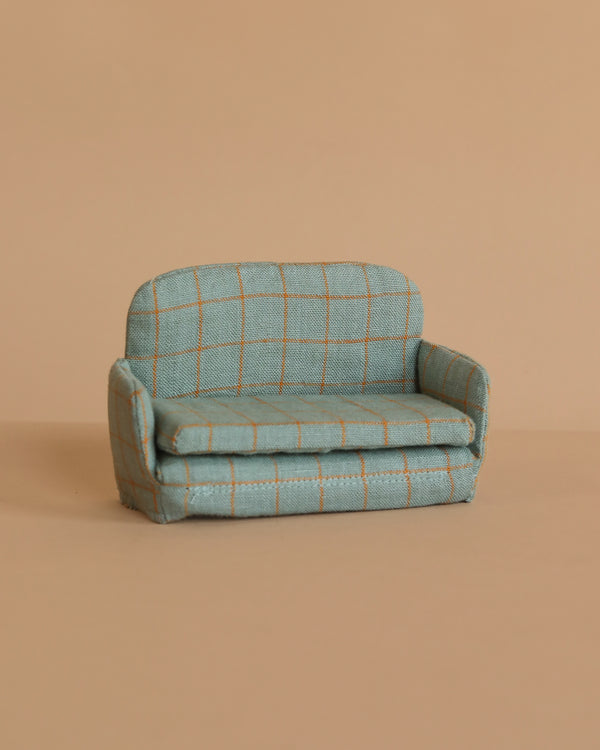 The Maileg Sofa Bed, Mouse - Checker is a small blue-green upholstered sofa with a checked pattern, displayed on a beige surface against a matching beige background.