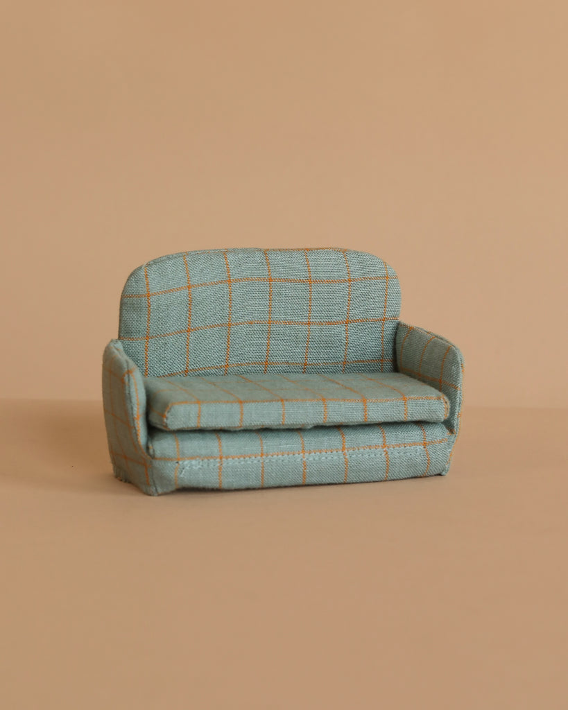 The Maileg Sofa Bed, Mouse - Checker is a small blue-green upholstered sofa with a checked pattern, displayed on a beige surface against a matching beige background.