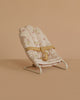The Maileg Babysitter, Micro - Off White features a small, padded seat with a floral pattern and yellow safety straps on a white metal frame. Perfect as baby doll furniture or for micro-sized rabbits; displayed on a beige surface and background.