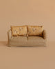 A small beige checkered Maileg Couch, Mouse - Mable, with two floral-patterned cushions, set against a plain beige background.
