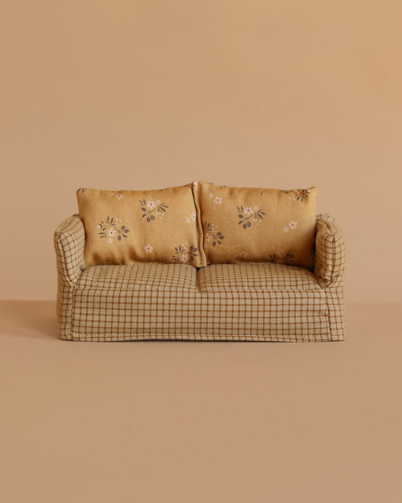 A small beige checkered Maileg Couch, Mouse - Mable, with two floral-patterned cushions, set against a plain beige background.