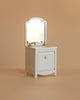 The Maileg Little Bother Bathroom Set—a small, white vintage-style vanity with a mirror and gold faucets—stands out against a beige background, making it an ideal match for Mouse Hole Farmhouse collection furniture.