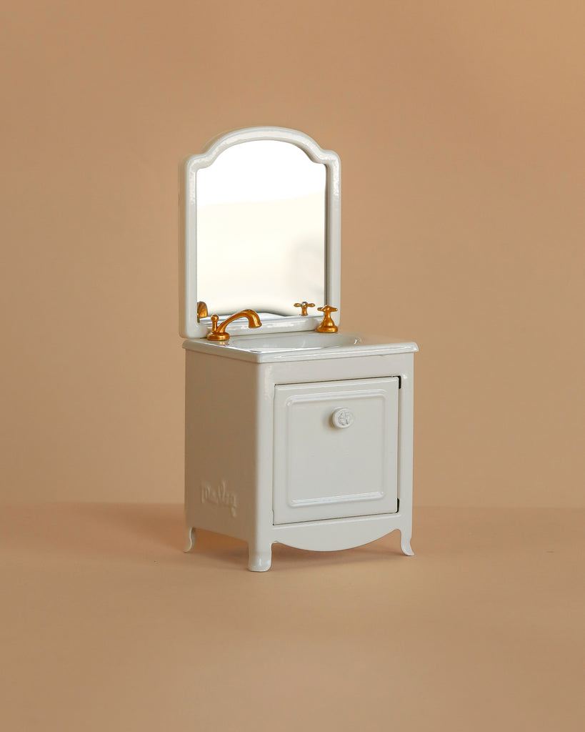The Maileg Little Bother Bathroom Set—a small, white vintage-style vanity with a mirror and gold faucets—stands out against a beige background, making it an ideal match for Mouse Hole Farmhouse collection furniture.