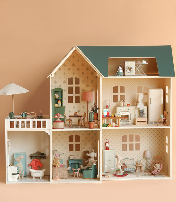 The Maileg Fully Furnished Dollhouse Set + Surprise Gift features five decorated rooms, a balcony, adorable furniture, and animal figurines—including a miniature bathroom—set against a peach background.