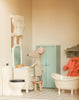 The Maileg Fully Furnished Dollhouse Set + Surprise Gift creates a cozy bathroom scene with a toy mouse in pajamas, dollhouse furniture like a toilet, bathtub, mint-green cabinet, tiled floor, mirror sink, and more charming mini details.