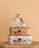 The Maileg Unicorn and Ballerina with Suitcase Set features a ballerina mouse on a unicorn, all displayed atop charming suitcases with animal and rainbow patterns, set against a beige background.