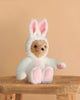 The Steiff Teddy Bear with Bunny Hoodie Costume, 11 inches, features a brown teddy dressed in a fluffy white bunny hoodie with pink ear and paw details, sitting on a wooden stool against a beige background.