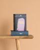 A "Moby Dick | Melville | Collector's Edition | Hardcover" stands upright on a wooden bench, with another copy of the same book lying flat beneath it against a plain light beige background.