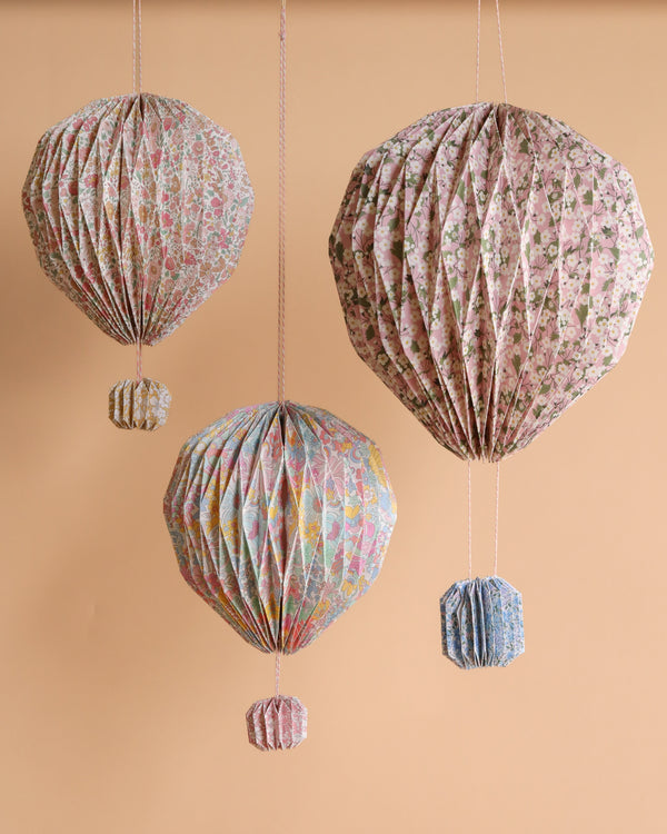 The Meri Meri x Liberty Origami Balloon Decorations feature three floral print balloons with matching paper baskets, hanging against a beige backdrop—ideal for adding charm to any baby shower.