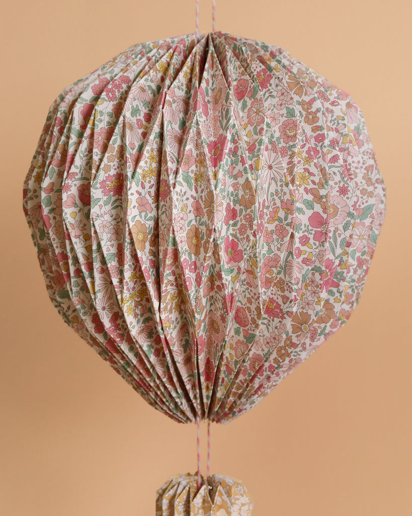 The Meri Meri x Liberty Origami Balloon Decorations feature a vibrant Liberty floral print in pink, green, and brown—ideal for adding charm to any nursery against a peach-hued backdrop.