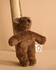 The Senger Naturwelt Stuffed Animal - Brown Bear, made from eco-friendly quality materials, features a white tag on its arm and leans against a wooden plank with a beige background.