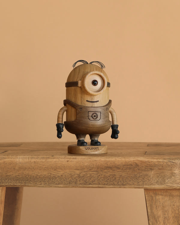 The Boyhood Minions Stuart, Small is a collectible figurine made from European FSC White Oak. It depicts one-eyed Stuart Minion with black gloves and hair, "STUART" inscribed on its base, and stands against a beige background.