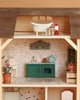 The Maileg Fully Furnished Farmhouse features an upstairs bathroom with a white bathtub and red lantern, plus a kitchen downstairs with floral wallpaper, green cabinet, blue teapot, blender, and charming mini accessories.