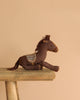 The Maileg Cowboy Set, featuring a brown plush horse with a patterned saddle, rests on a wooden bench against a simple beige backdrop.