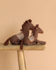 Two Maileg Pony, Medium stuffed toys in brown, made from soft cotton/linen with patterned backs, are displayed on a wooden bench against a plain beige background.