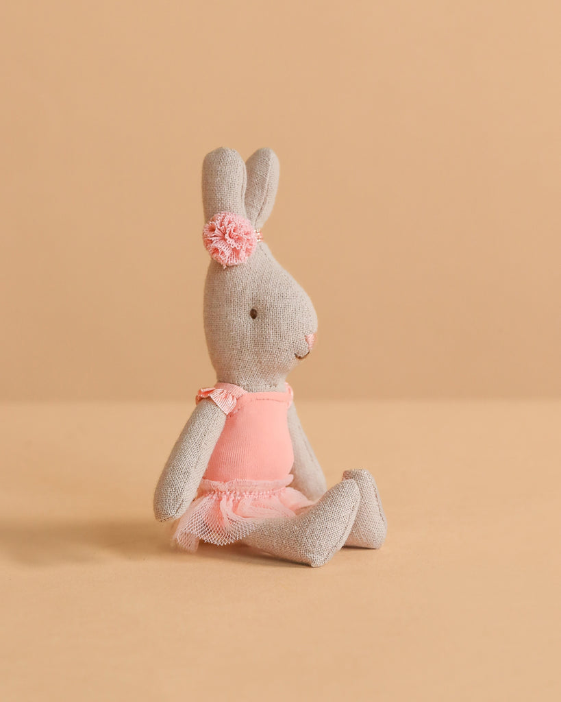 A Maileg Rabbit, Micro - Ballet Suit And Skirt, Rose sits against a beige background, dressed in a rose ballet suit and skirt with a matching headband.