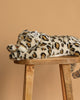 The Steiff XL Parddy Snow Leopard 21" is a lifelike plush toy with spotted fur, shown stretched out on a wooden stool against a plain beige background.