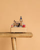 The London Music Box, featuring iconic London landmarks such as Big Ben, a red bus, and a phone booth, sits on a wooden stool against a plain beige background.