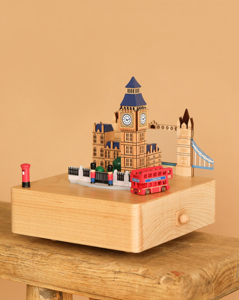 The London Music Box features miniature models of Big Ben, Tower Bridge, a red bus, and a postbox on a light wooden base—an ideal decorative piece for any music box collection.