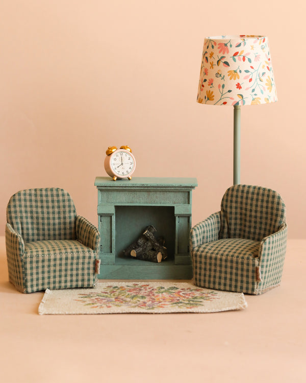 The Maileg Living Room Starter Set includes two green plaid chairs, a teal fireplace with a tiny clock, floral lampshade, and rug—perfectly sized for Maileg mice—all set against a light beige background.