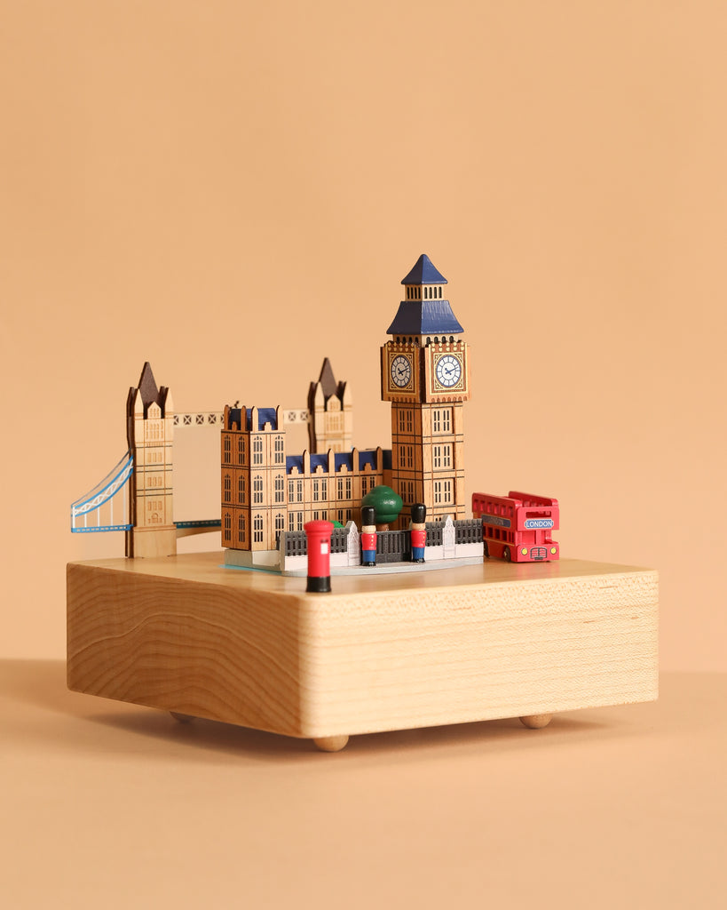 The London Music Box is a decorative wooden piece showcasing Big Ben, Tower Bridge, and red double-decker buses on a light wood base with a beige background.