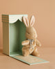 The Maileg My First Bunny - Brown, a small plush bunny with a ribbon bow, sits in front of an open mint green striped gift box on a beige background—an adorable surprise for any occasion.