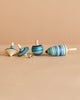 The Mader Spinning Top Champion Learning Set - Ice features five fun tops in various shapes and sizes with blue and green stripes, arranged upright and on their sides on a beige surface—ideal for beginner to advanced spinners.