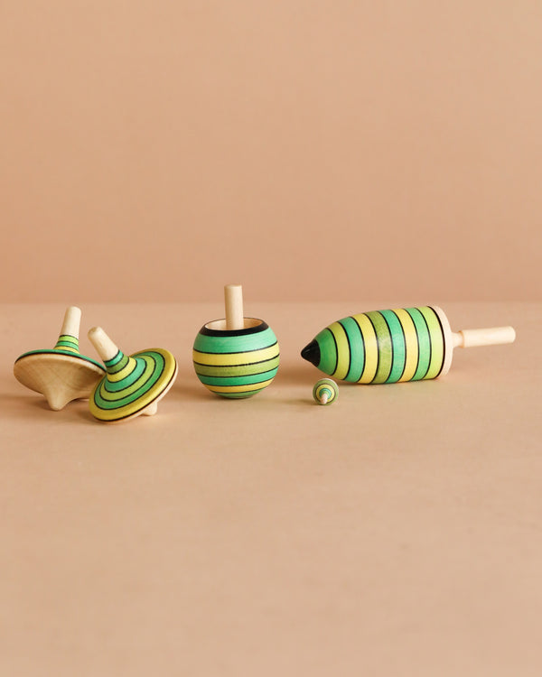 The Spinning Top Champion Learning Set - Grass includes four wooden tops in different shapes and sizes with green and yellow stripes, perfect for all skill levels and adding a playful touch to any room.