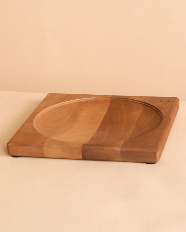 The Walnut Wood Spinning Plate is a square plate with a central round, shallow indent and natural wood grain, crafted to meet toy safety standards. It is displayed on a light beige surface with a matching background.
