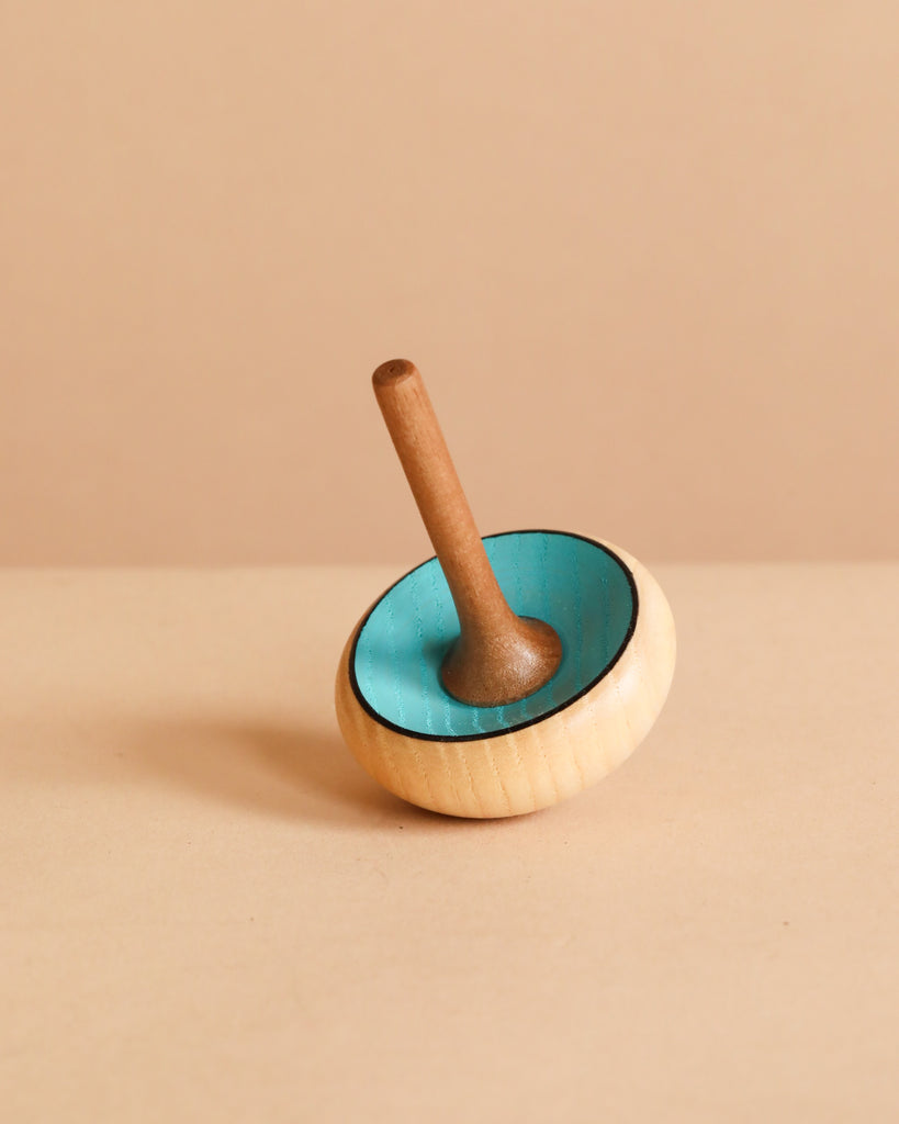 The Mader Zwirbel Spinning Top - Blue, made from Walnut and Ash with a blue interior and natural wood exterior, stands upright on a light beige surface against a beige background.