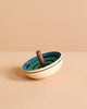 The Mader UFO Flora Spinning Top - Blue, crafted from maple wood with a dark handle and ombre green and blue concentric circles, rests on a beige surface against a coordinating beige background.